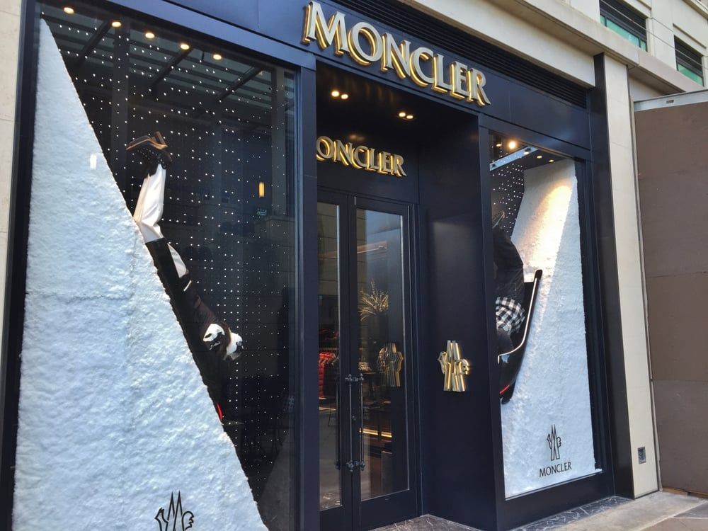 Moncler store exterior with black and gold sign, display window with white accents.