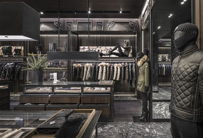 Luxury clothing store interior with mannequins, racks of jackets, dark wood display cases, and decorative lighting.