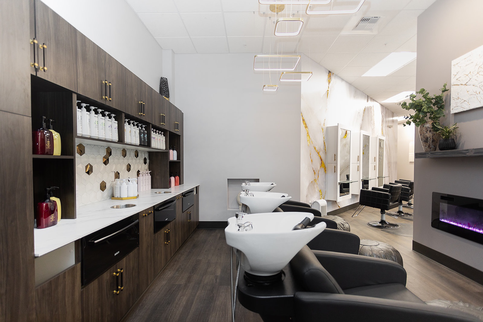 Hair salon interior with dark cabinetry, white countertops, and wash stations.