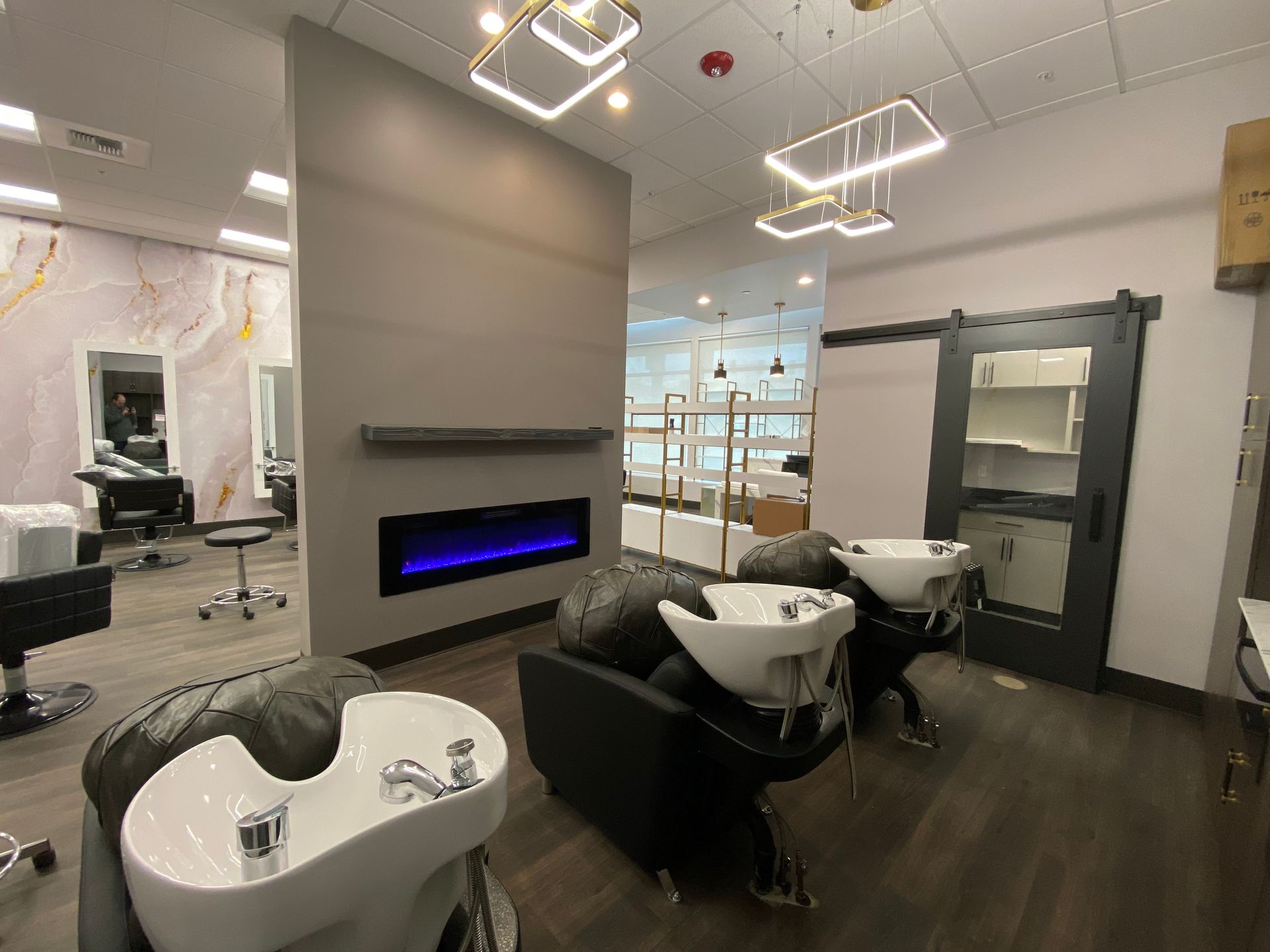 Hair salon interior with shampoo stations, a fireplace, and modern lighting.