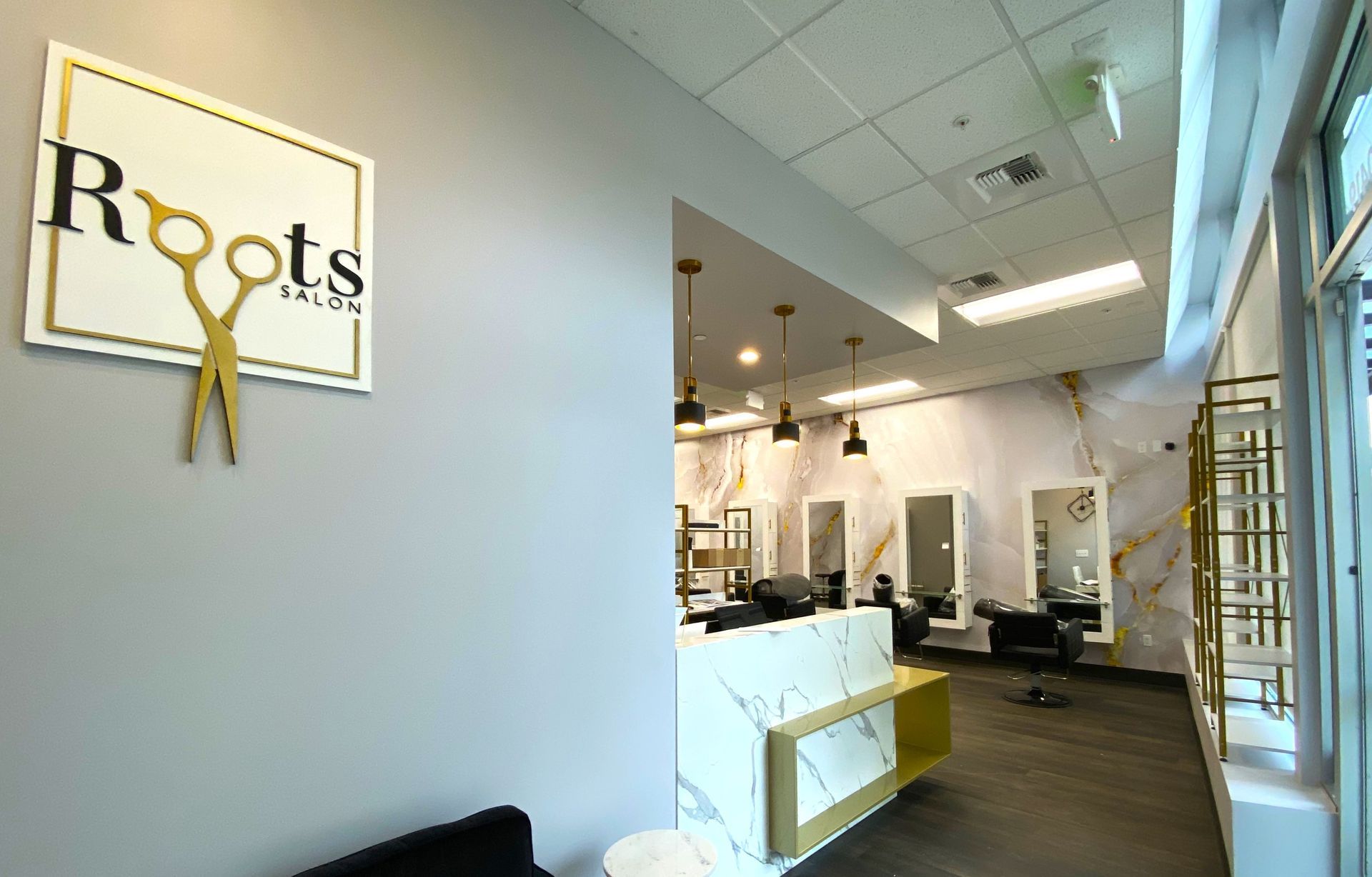 Interior of Roots Salon with sign, marble counter, mirrors, and stylists' stations.