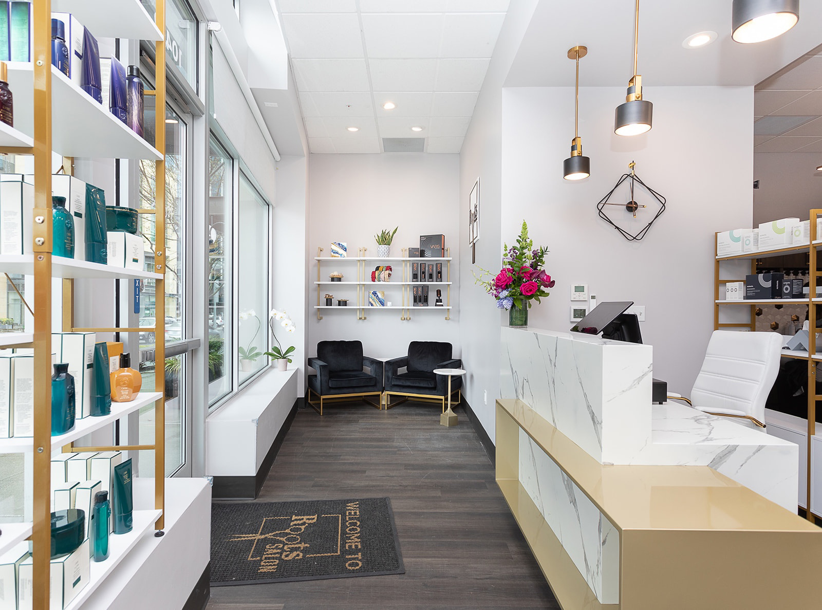 Hair salon interior with product displays, reception desk, seating area, and floral arrangement.