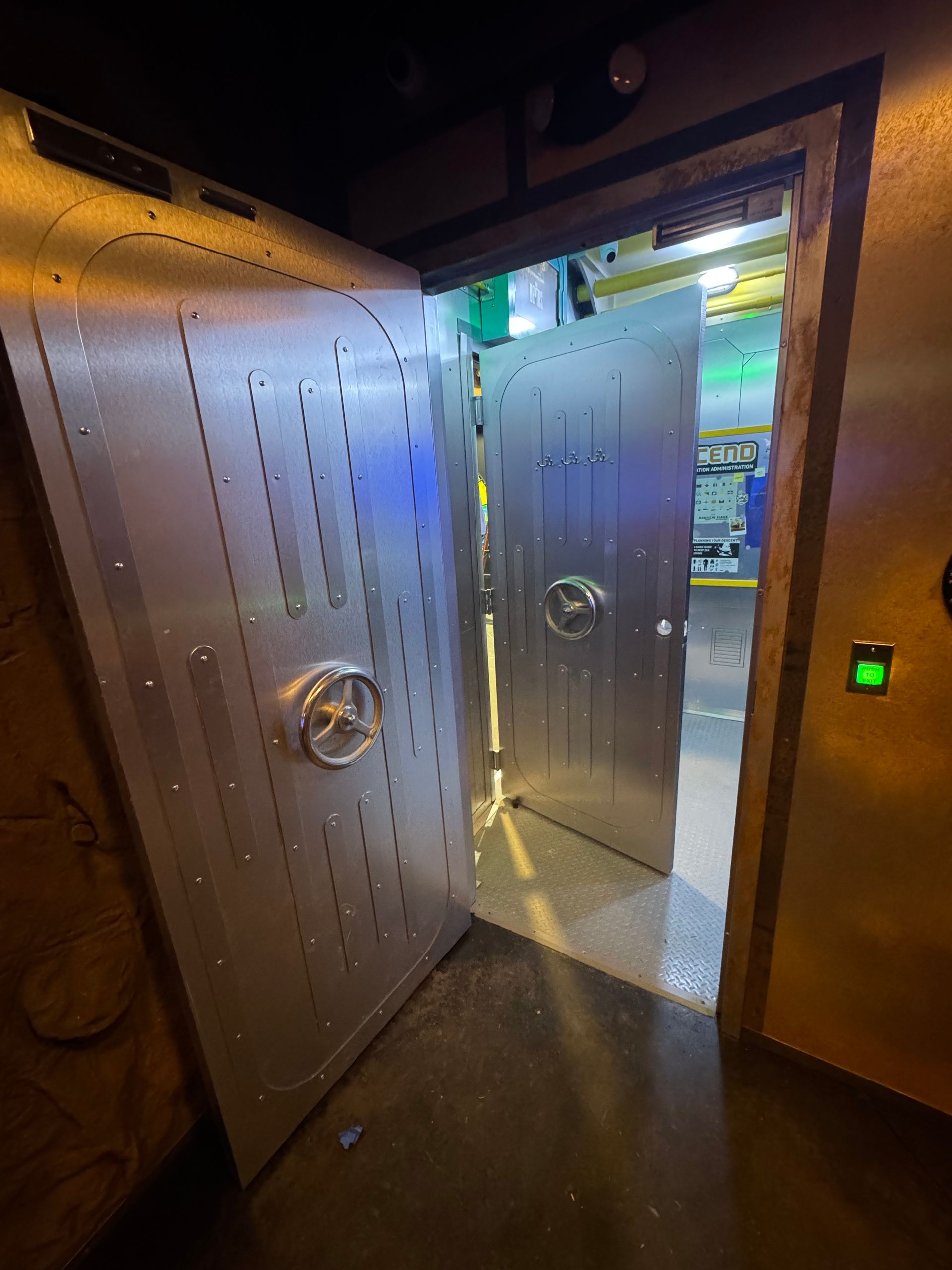Open, silver vault doors with round handles, doorway to a brightly lit area.