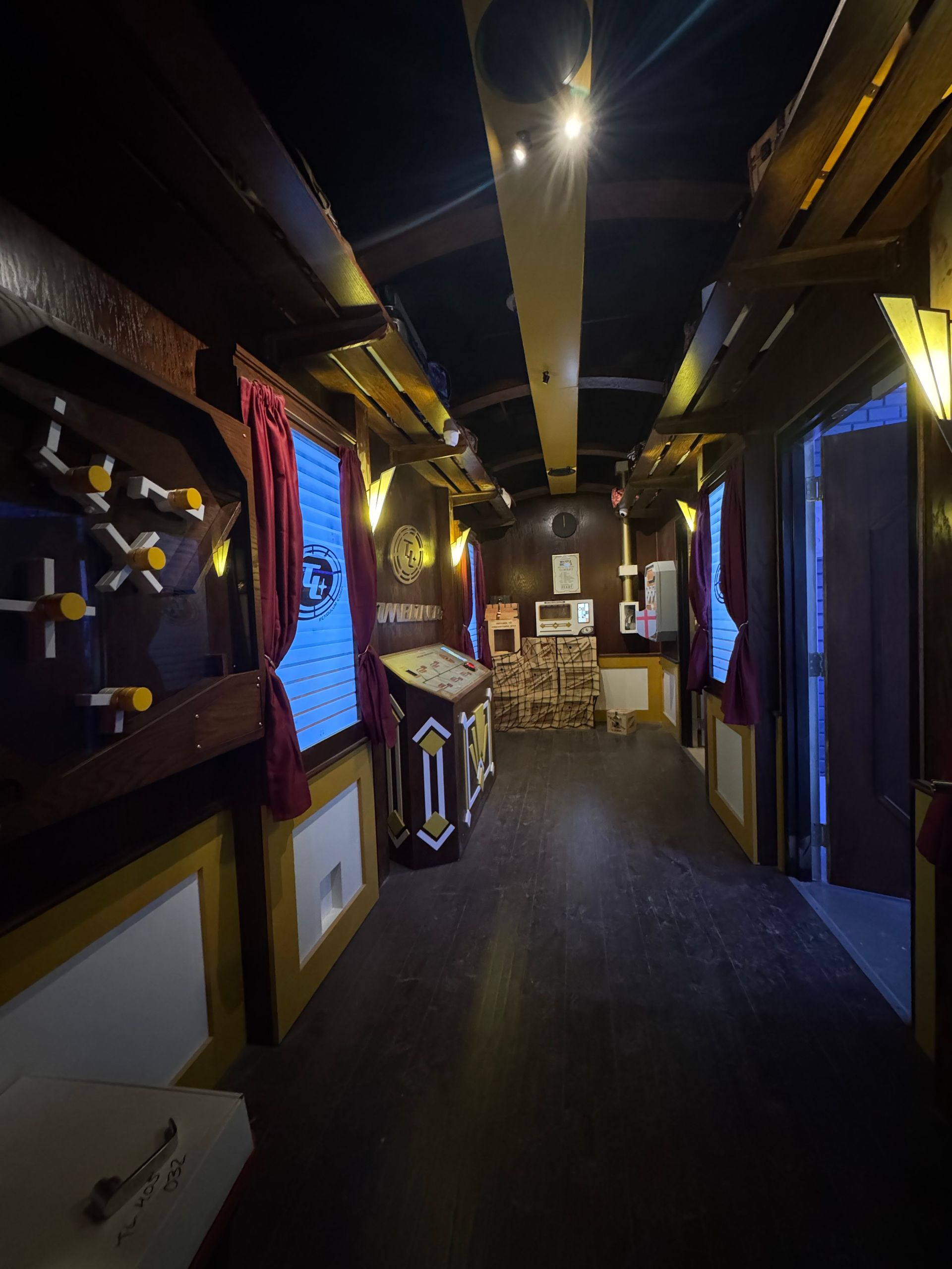 Long hallway in a themed room with dark wood paneling, red curtains, and props.