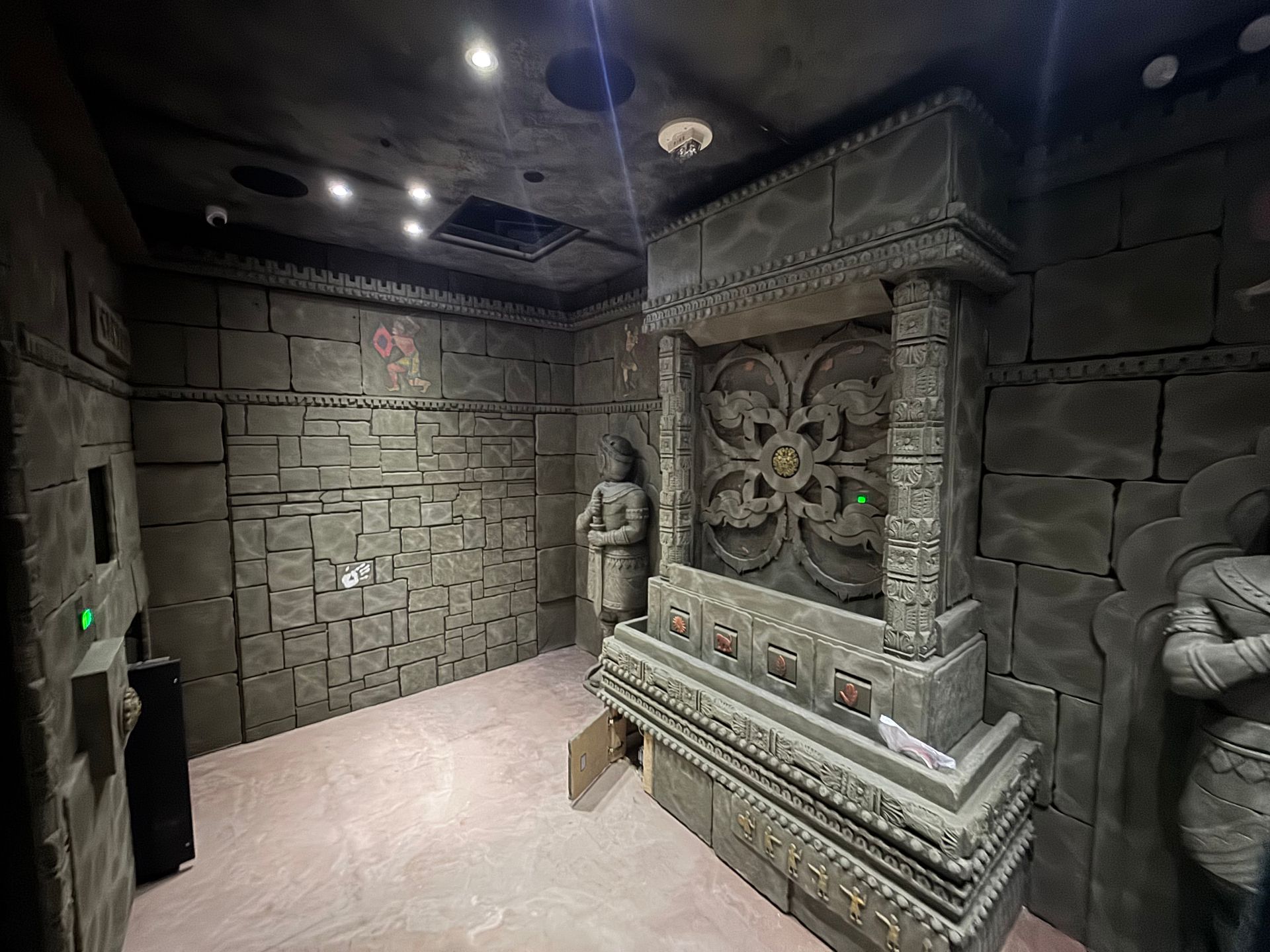 Stone room with ornate carvings, two statues, and a central decorative structure.