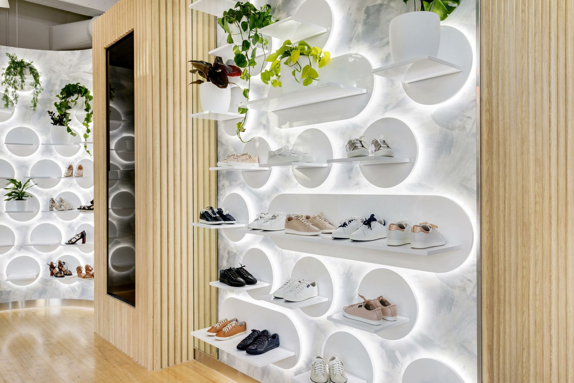Shoe display in store with backlit circular shelves holding shoes and plants. Wooden paneling.