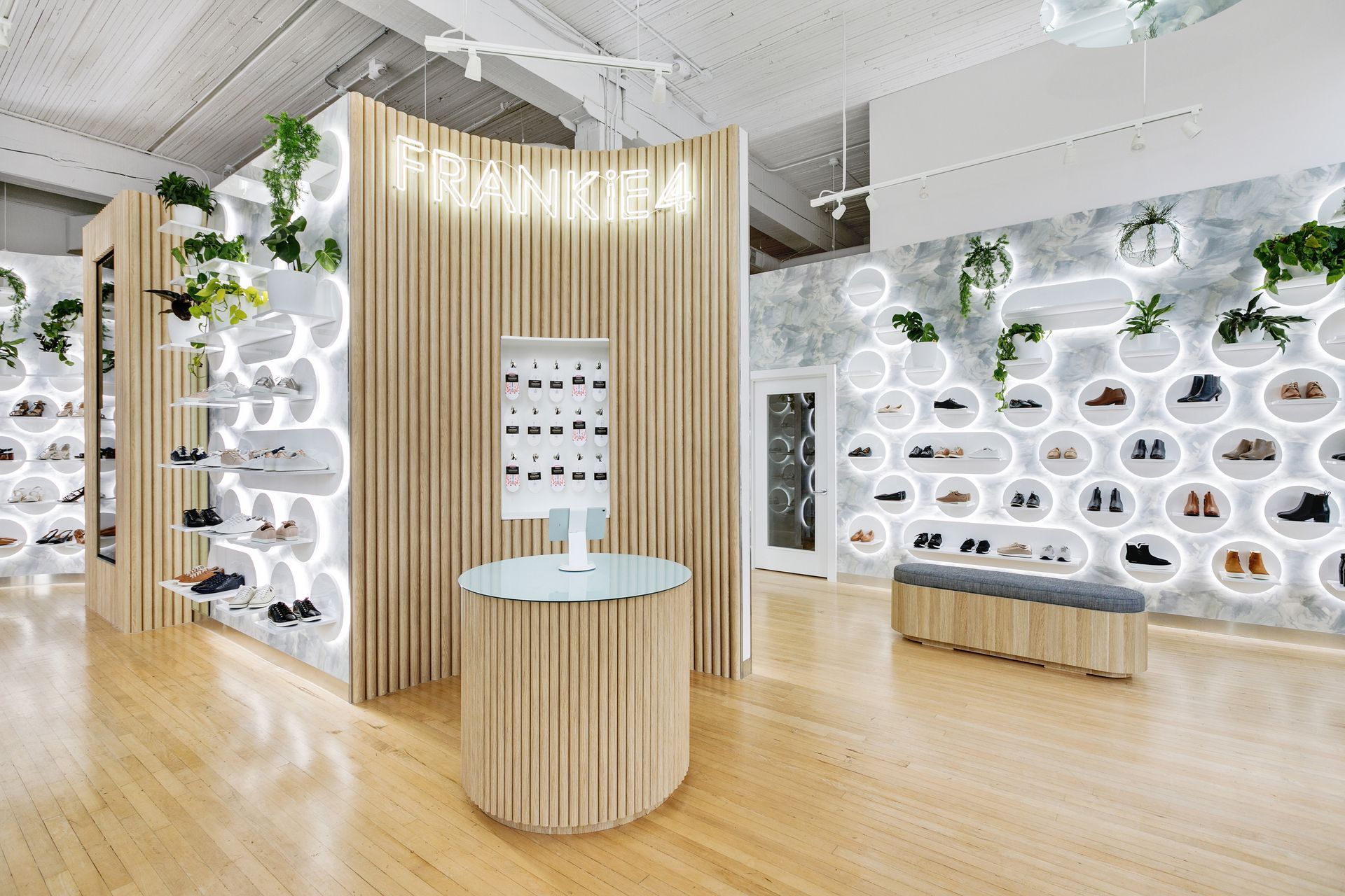 Shoe store interior with wooden shelving, illuminated circles, and plants. Shoes displayed on shelves.