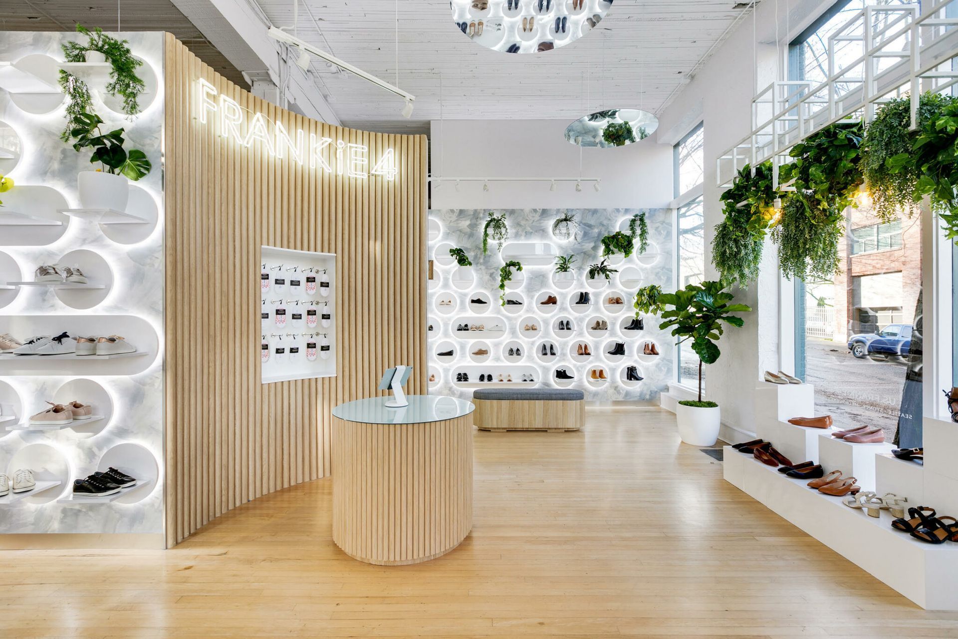 Shoe store interior with wooden display, shelves with shoes, hanging plants, and large windows.