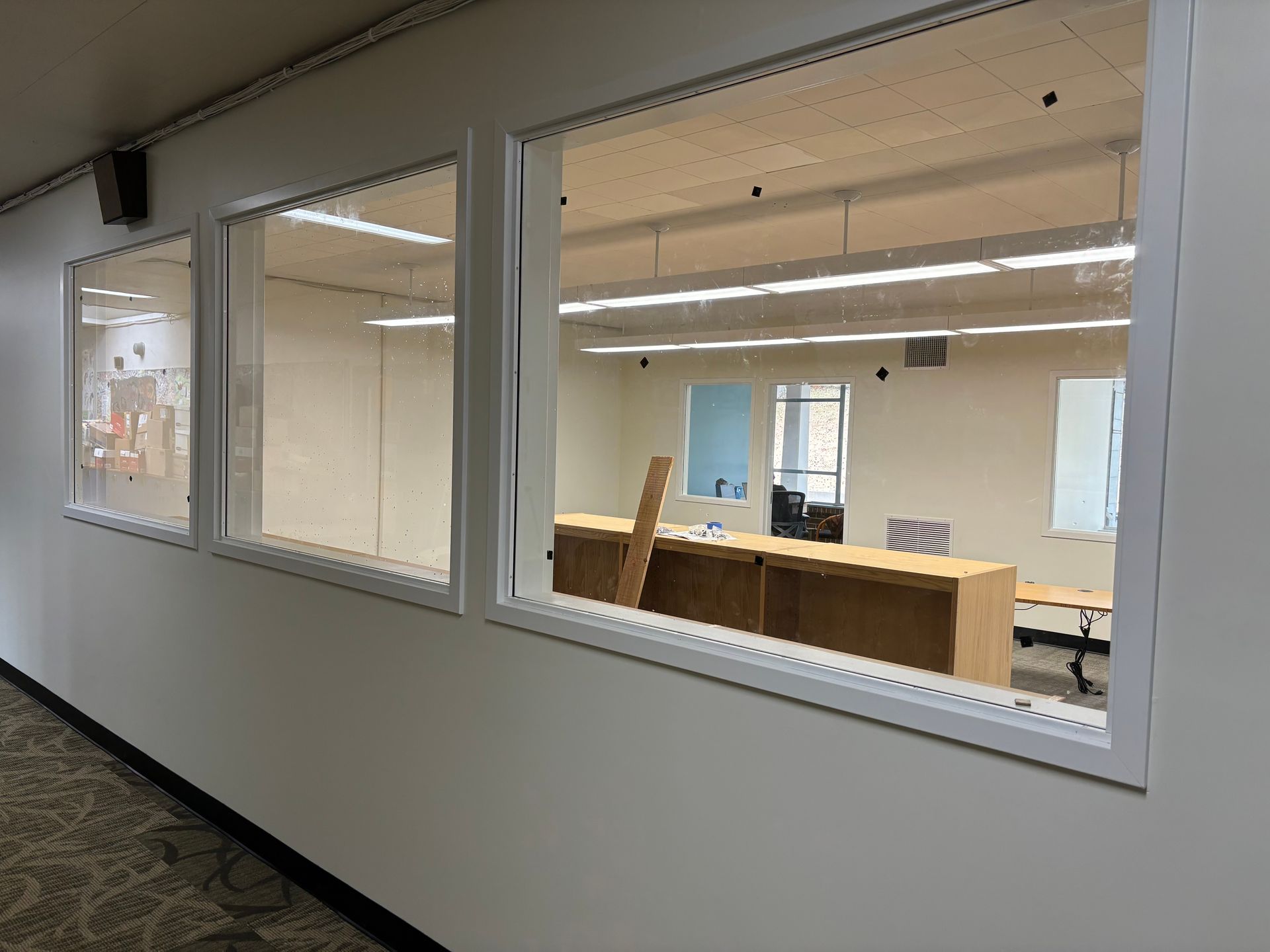 Three windows in a white wall, looking into an empty office with desks and windows.