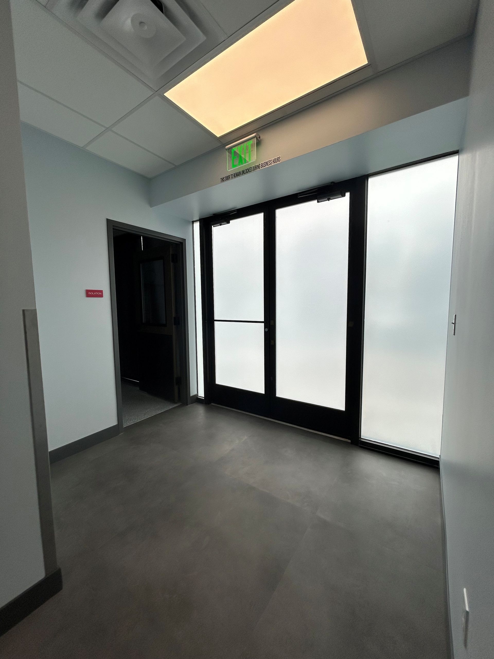 Hallway with closed doors and emergency exit sign above the frosted glass doors.