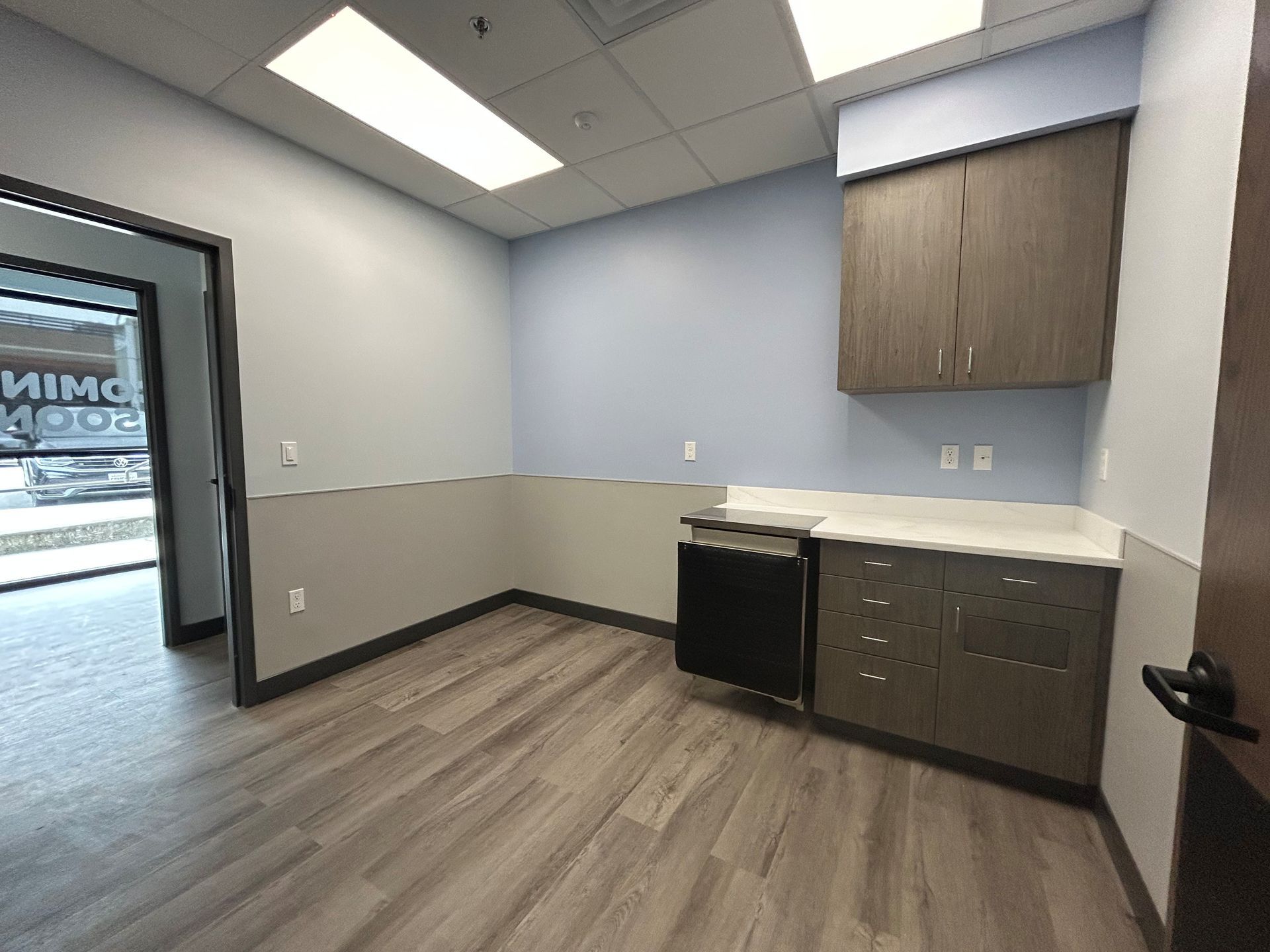 Empty office interior with light wood flooring, gray walls, and built-in cabinets.