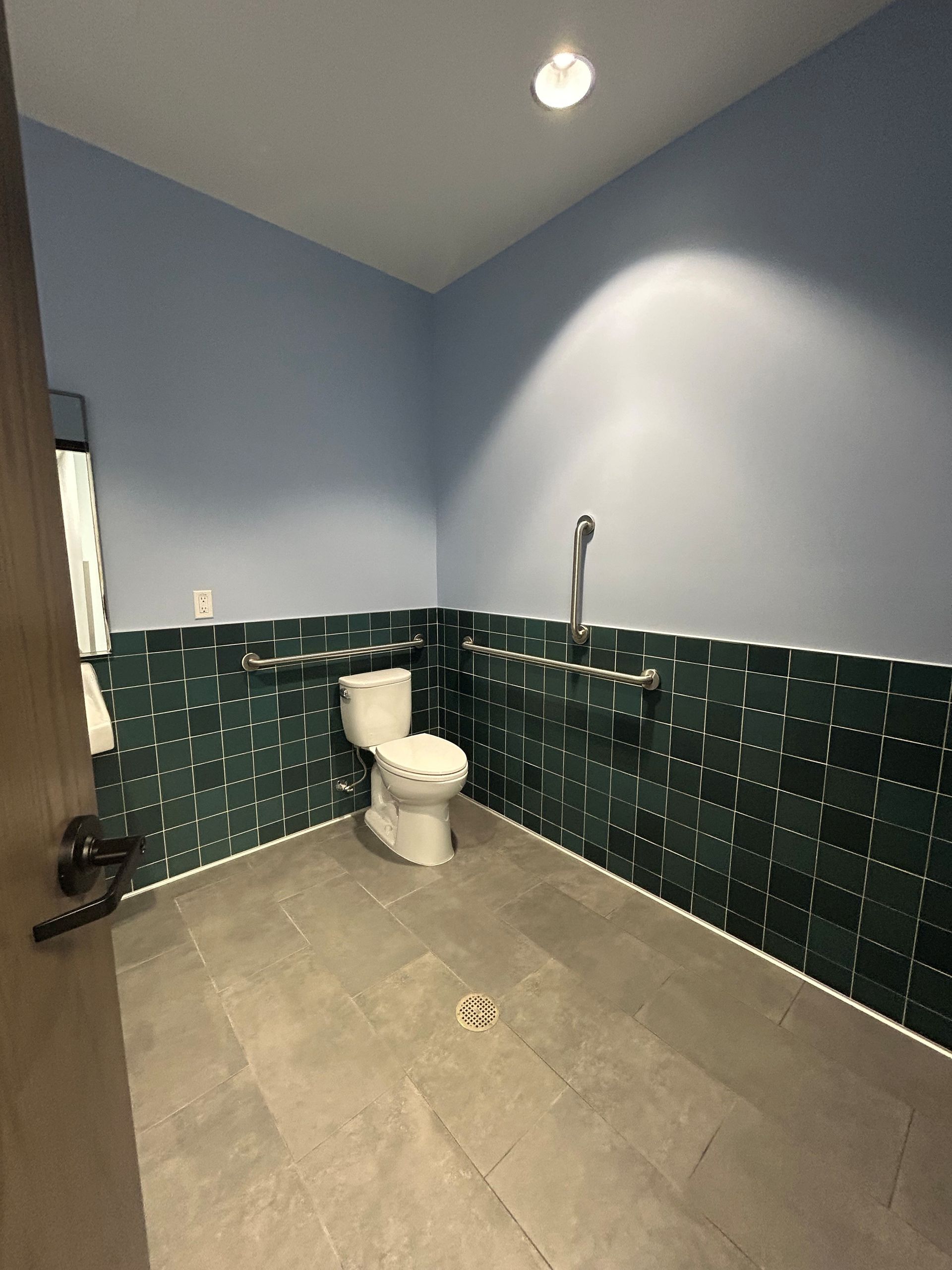 Accessible bathroom with toilet, grab bars, and showerhead on blue-green tiled wall.