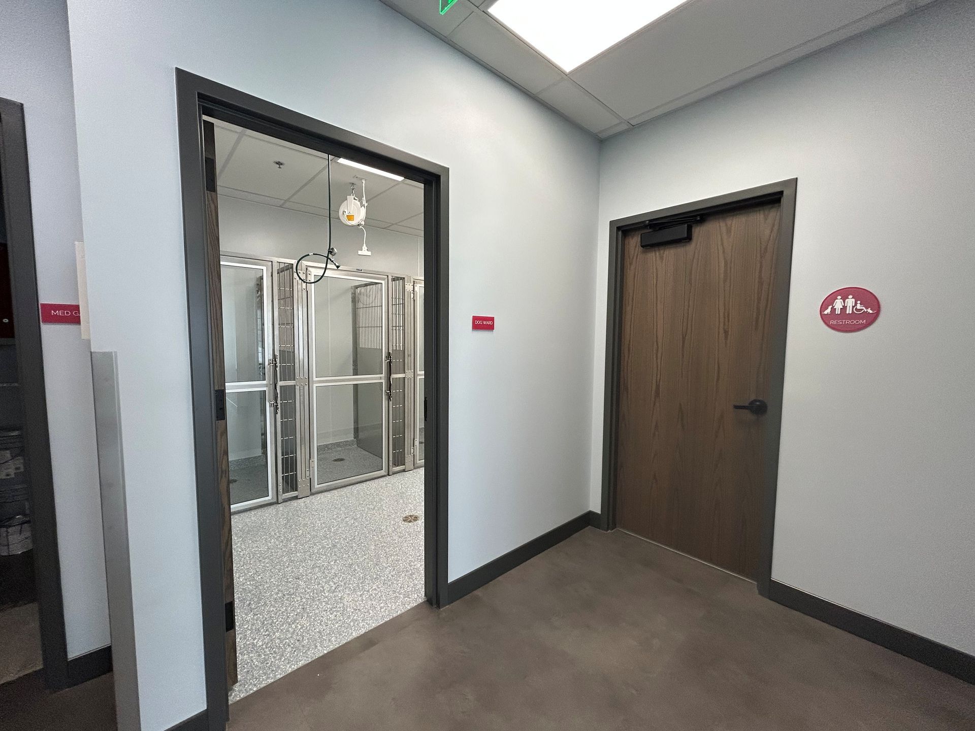 Hallway with open door to a room with metal cages, another door to the right, and a red sign on the wall.