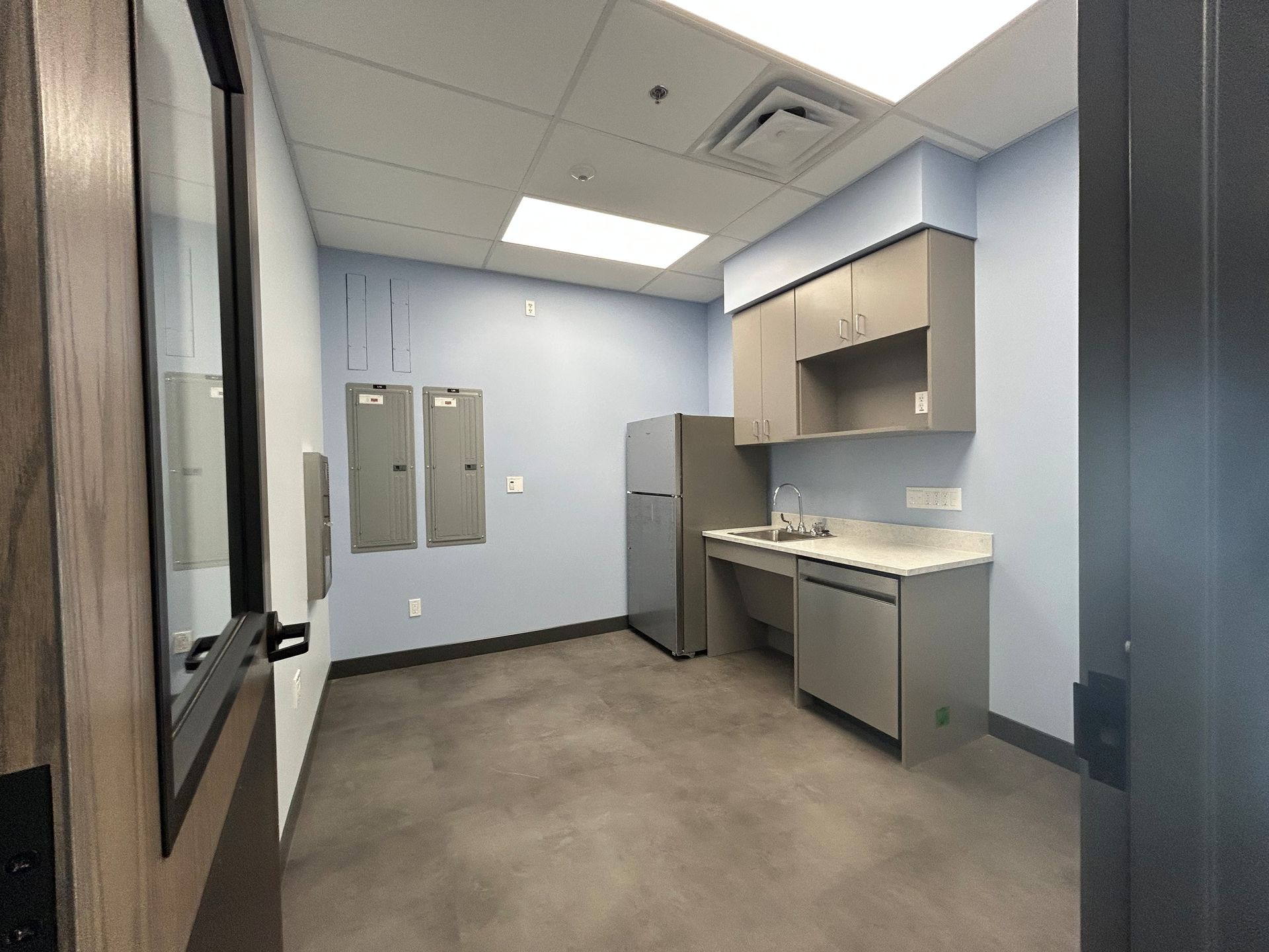 Small office kitchen with cabinets, refrigerator, sink, and grey flooring.