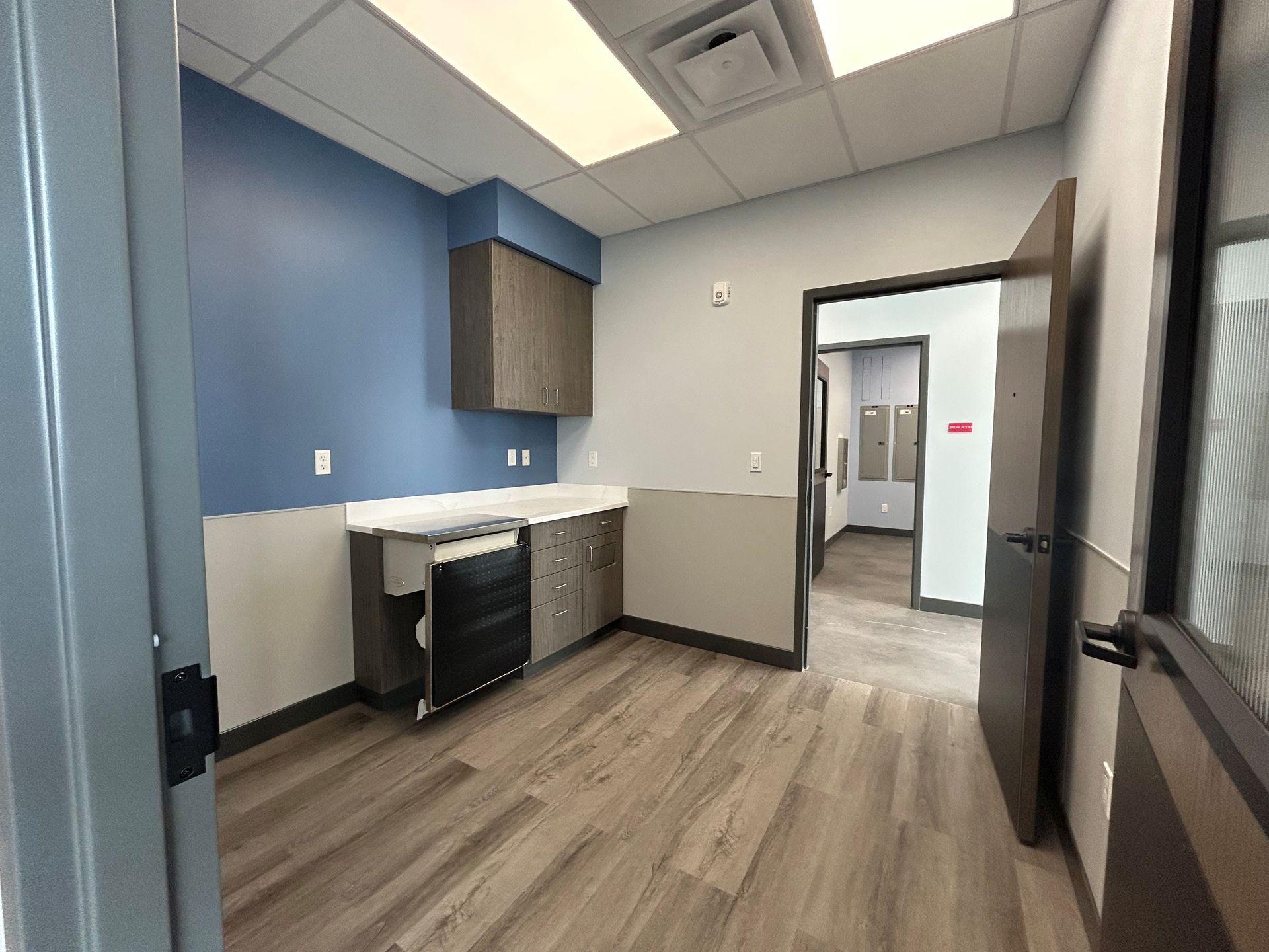 Empty office space with blue, gray, and wooden accents, cabinets, and open doorway to hallway.