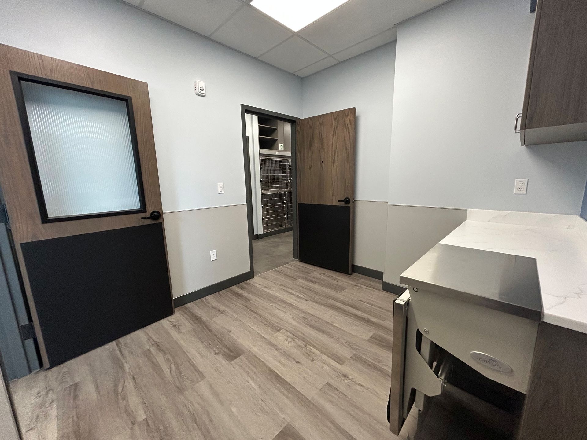 Empty office interior with wood-look flooring, two-tone walls, and a desk. Two doors lead to other rooms.