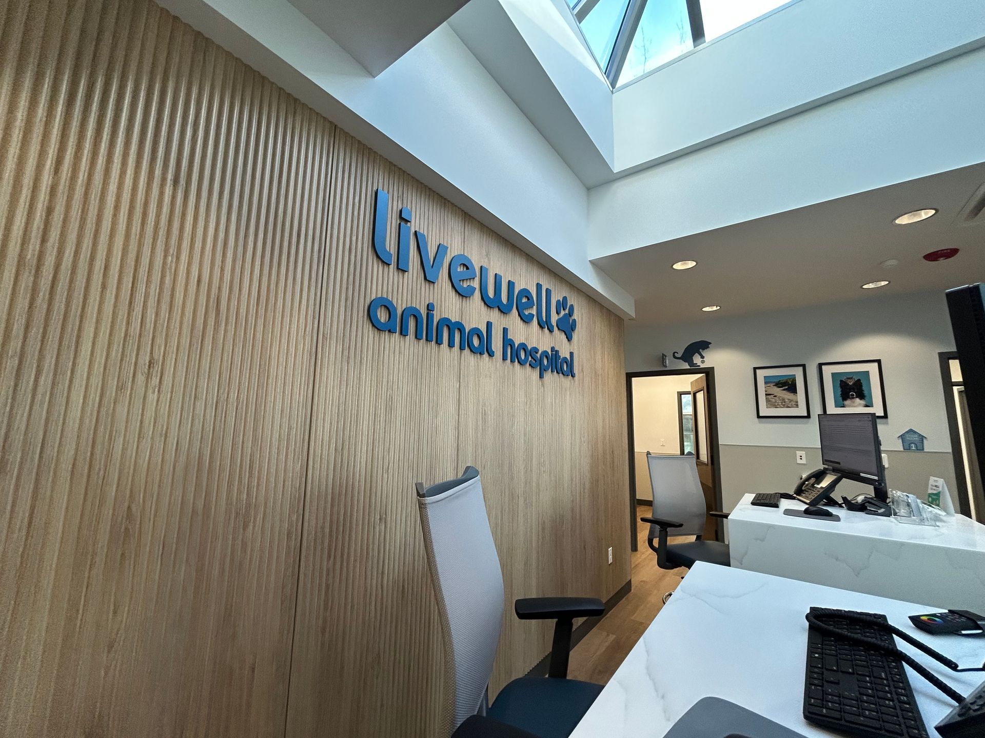 Livewell Animal Hospital sign on wood-paneled wall, interior view. Reception desk, chairs, and skylight visible.