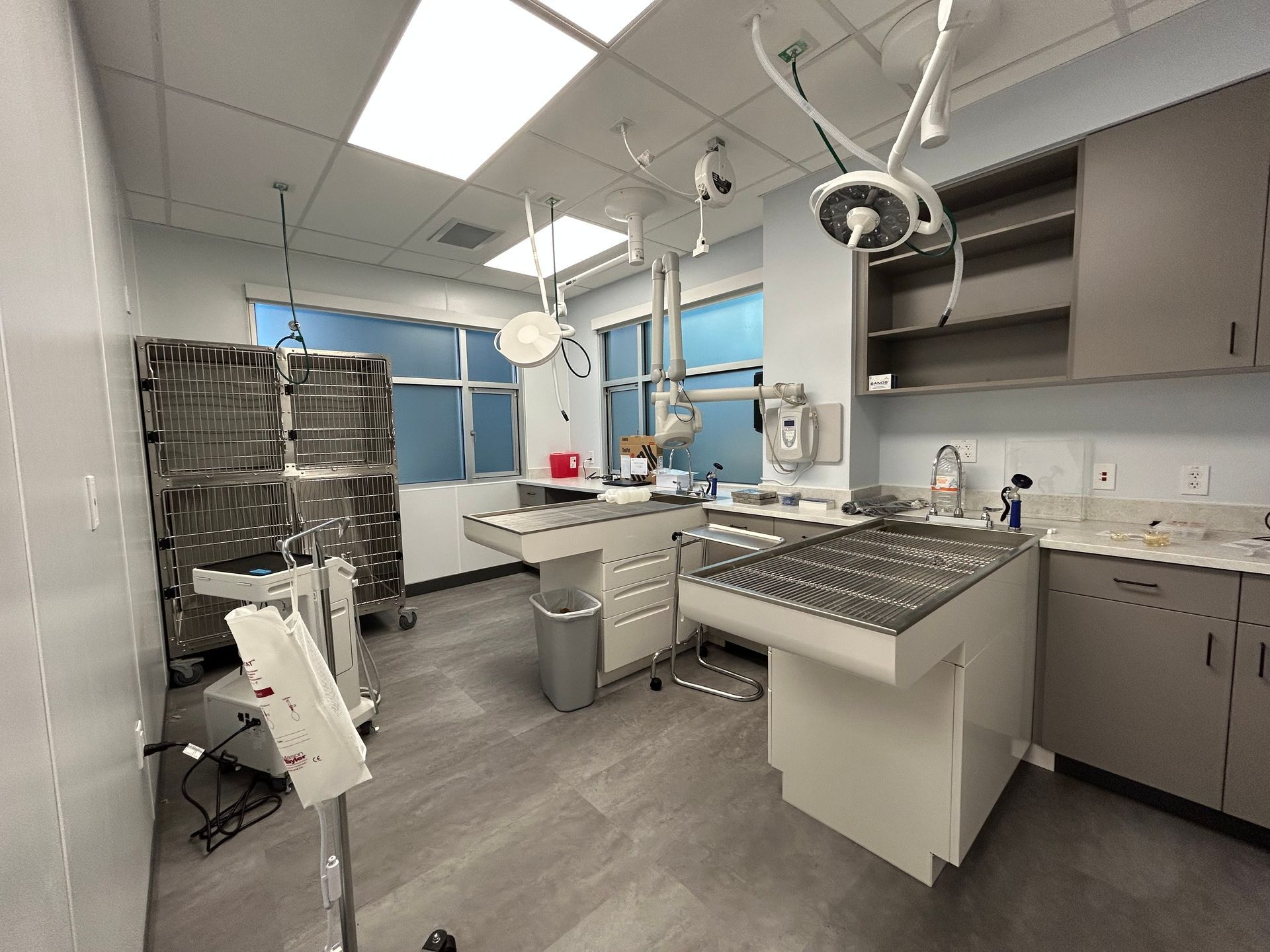 Veterinary surgery room with surgical tables, overhead lights, stainless steel storage, and cabinets.