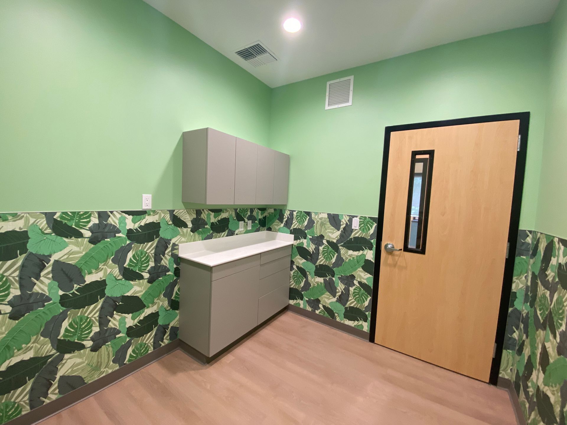A small room with light green walls, gray cabinets, a door, and tropical leaf wallpaper.