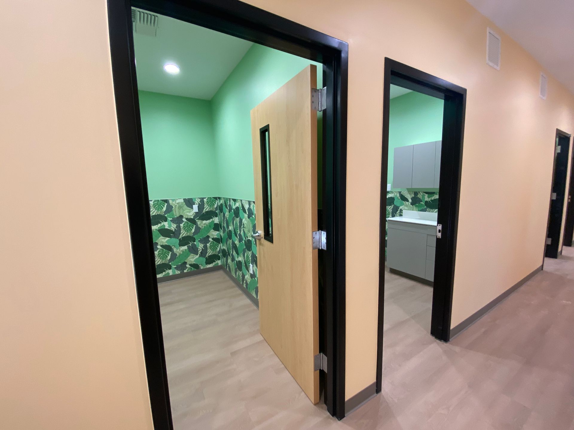Hallway with open doors to rooms with green and neutral-colored walls.