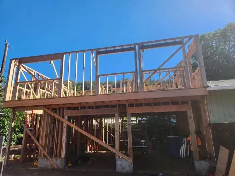 Two-story wooden building under construction against a blue sky; framing visible with windows.