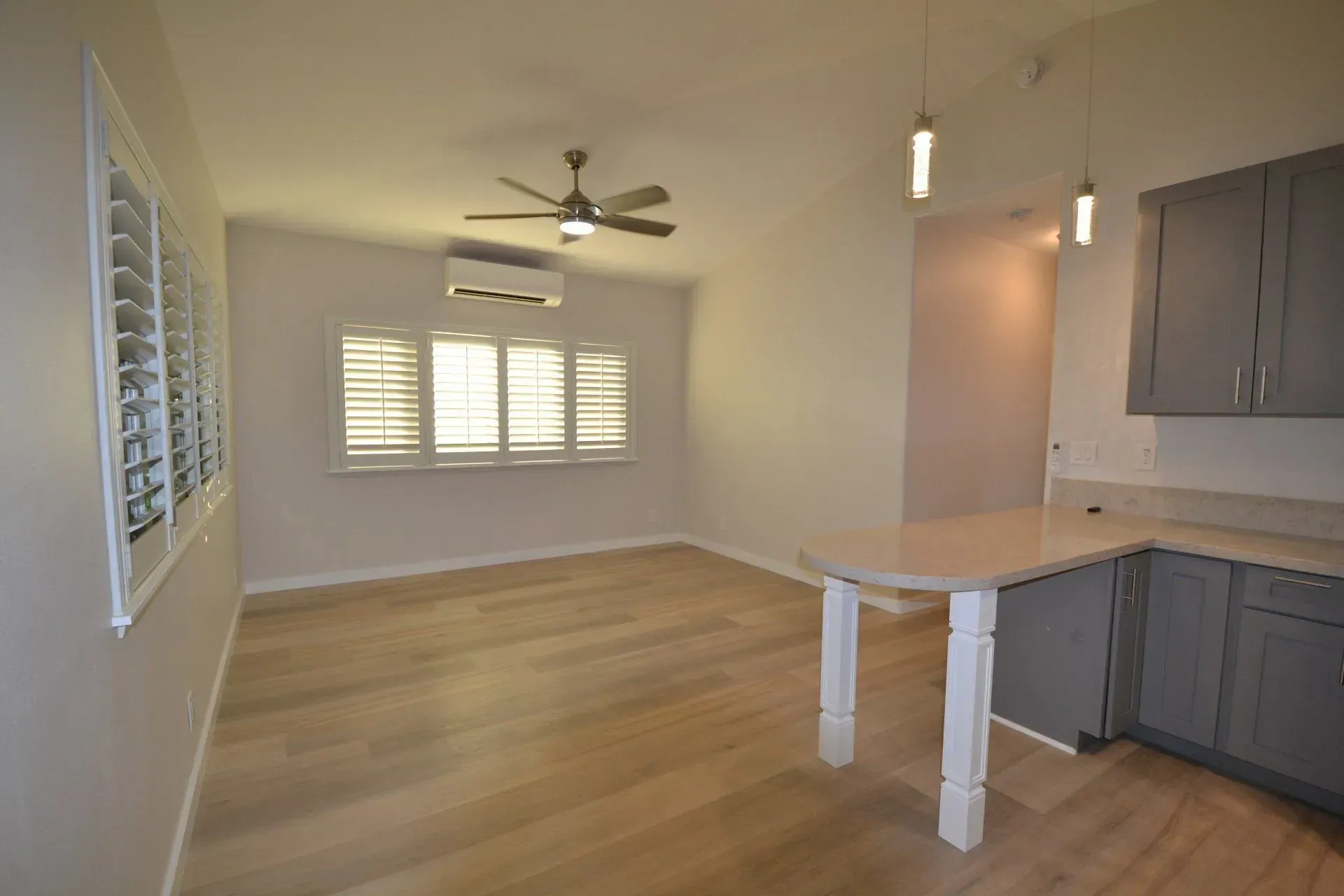 Bright dining area with light wood floors, gray cabinets, white countertop, and window shutters.