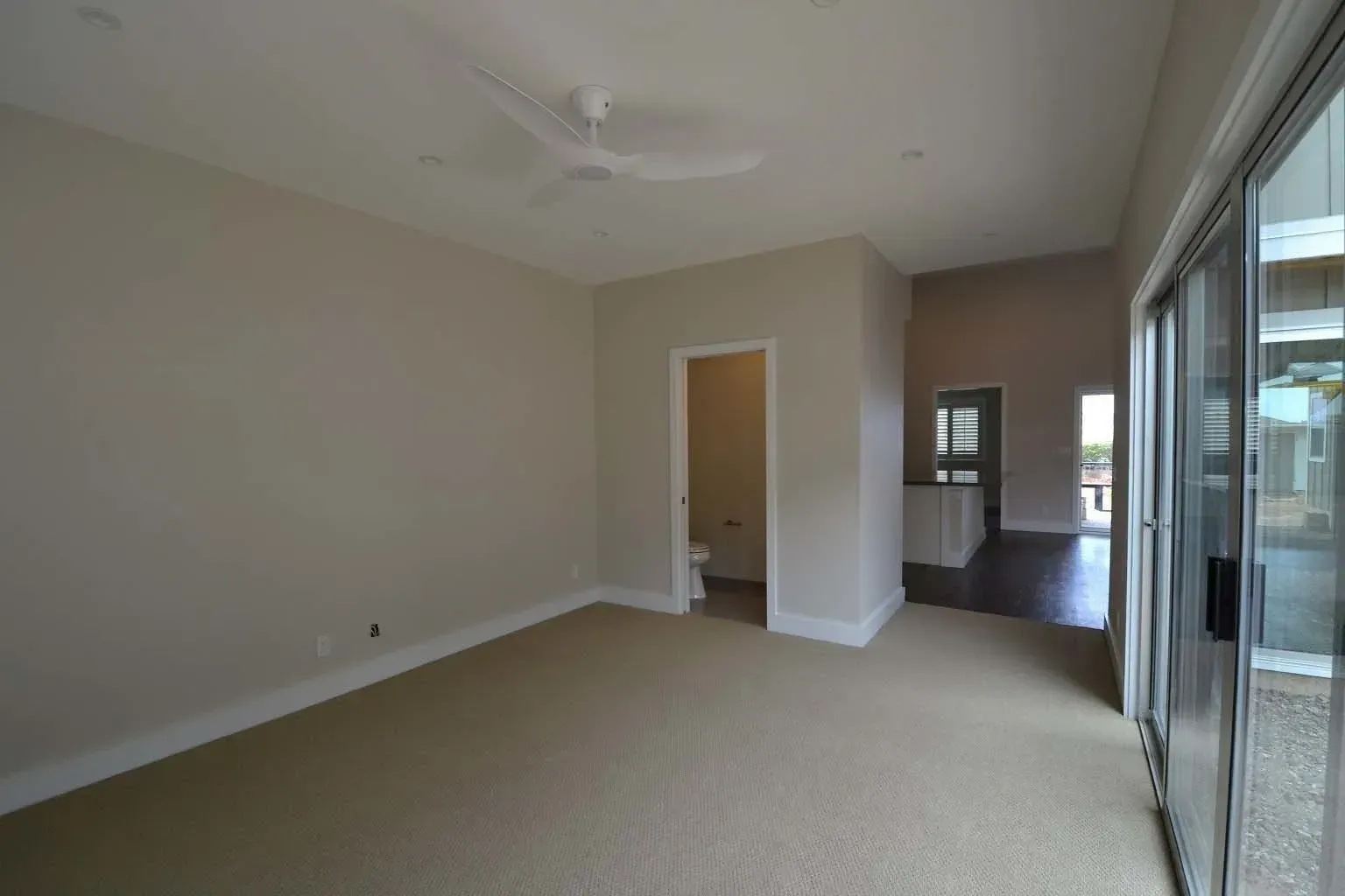 Empty room with beige carpet, light walls, sliding glass door, and doorway to a toilet.