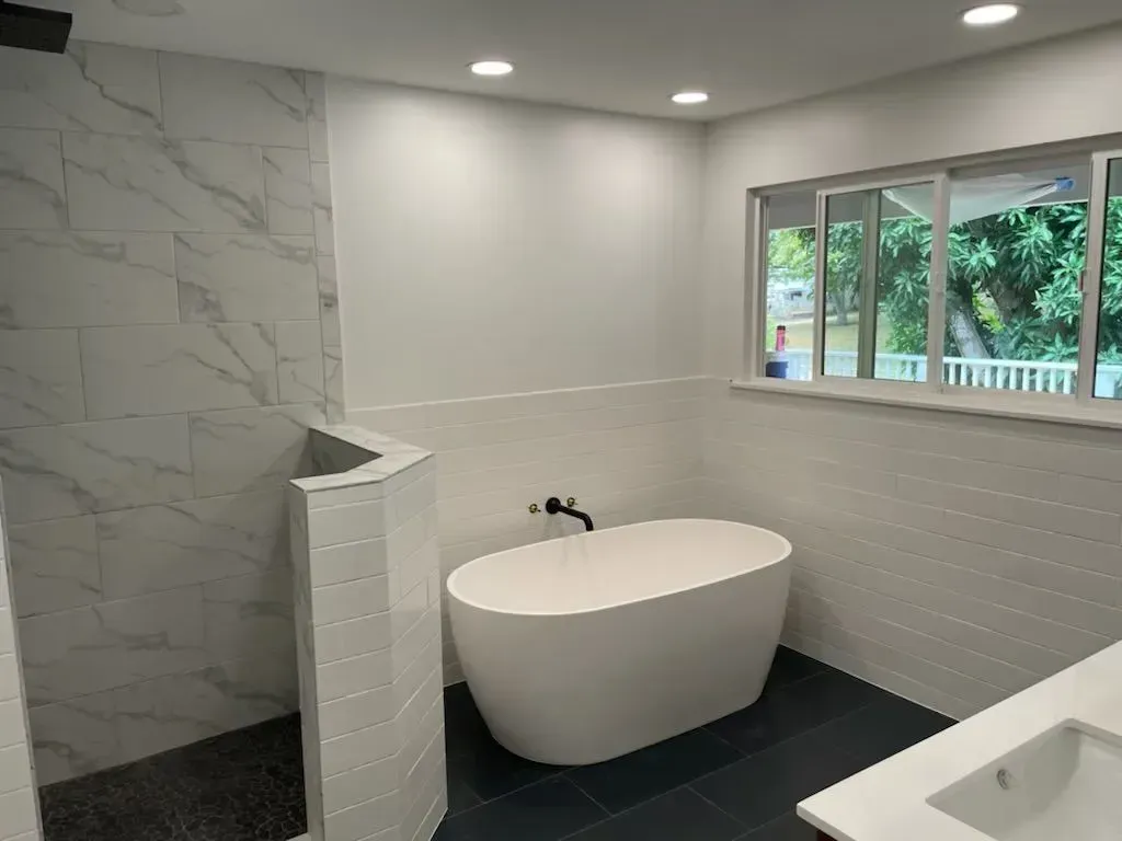 Modern bathroom with white walls, shower with marble tile, soaking tub, and window.