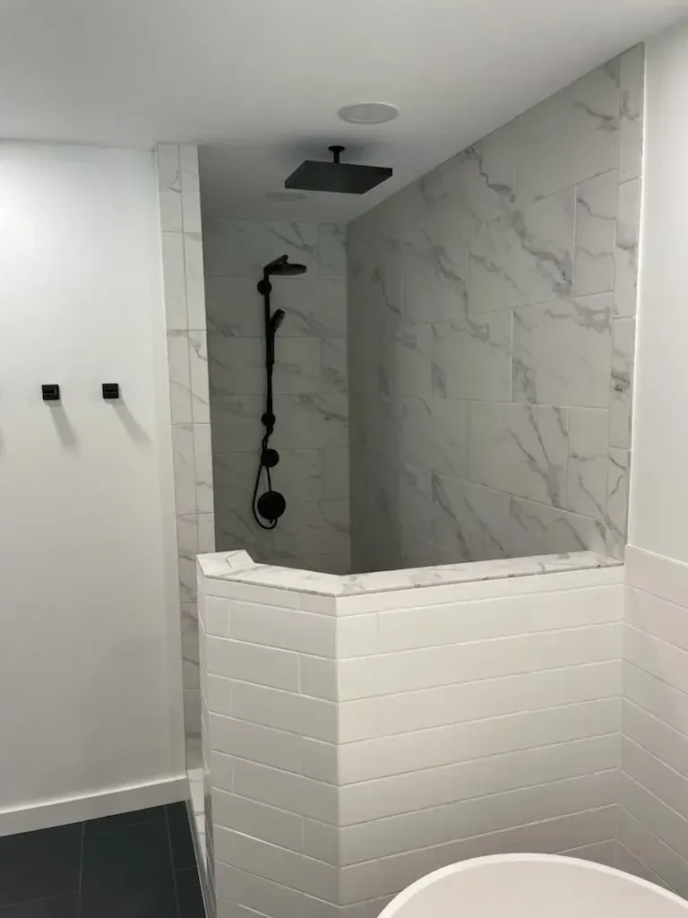 Modern shower with black fixtures and marble-look tile. White walls, curved entry.