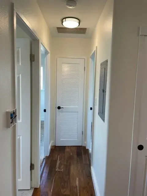 Narrow hallway with hardwood floor, white doors, and a ceiling light.