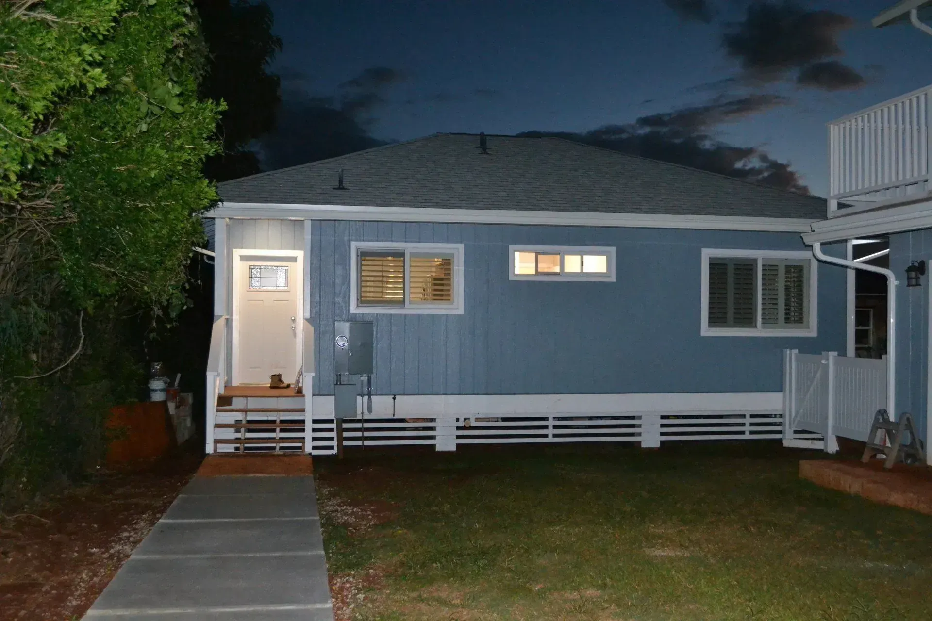 Blue house exterior at dusk with a white door, windows, and foundation. Concrete path and green lawn.