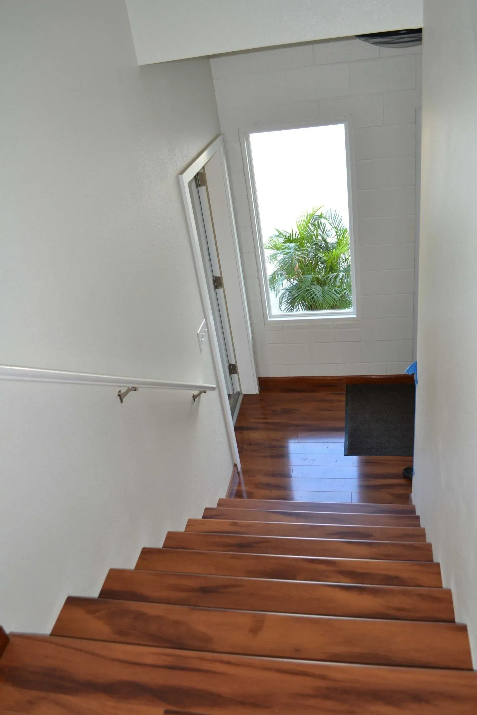 Wooden stairs leading down, with a white wall and a window at the top.