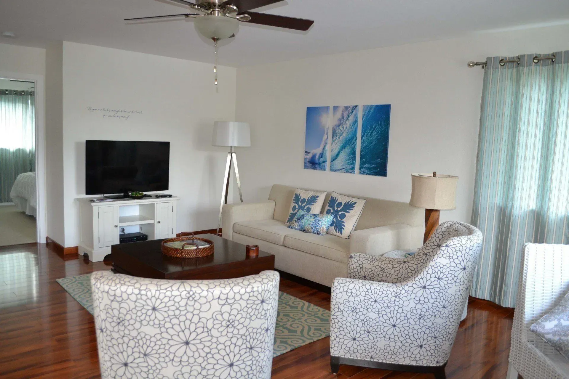 Living room with white walls, wood floor, white sofa, patterned armchairs, and ocean-themed artwork.