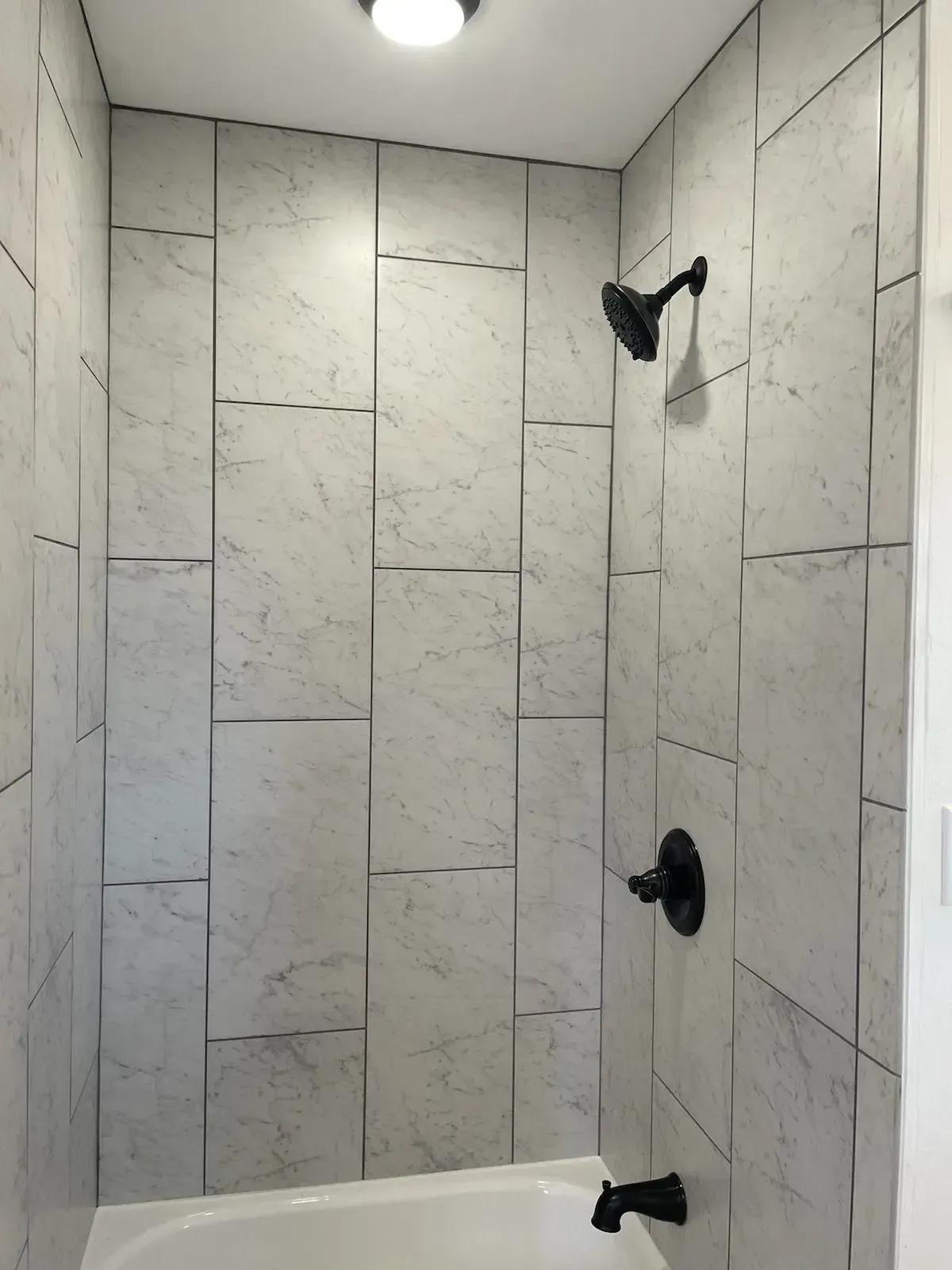 Tiled shower with black showerhead, faucet, and tub spout. White and gray marble-like tiles.