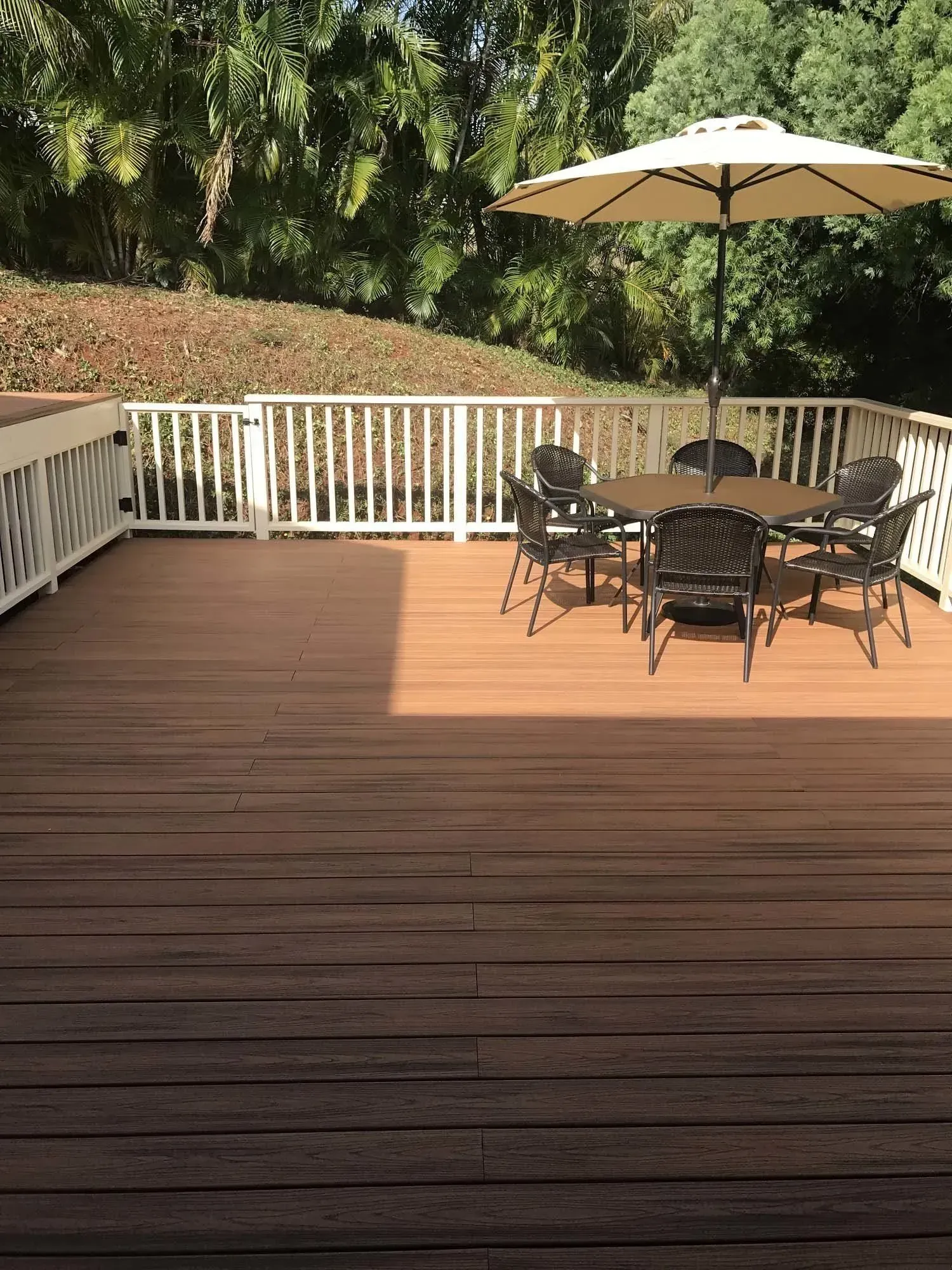 Wooden deck with outdoor furniture under a beige umbrella; trees in the background.