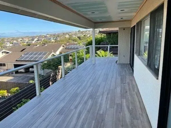 Deck with gray tiled floor, cable railing, and a view of a hillside neighborhood with solar panels.