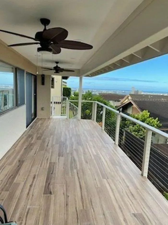 Covered deck with wood-look tile flooring, overlooking a city and ocean. Two ceiling fans.