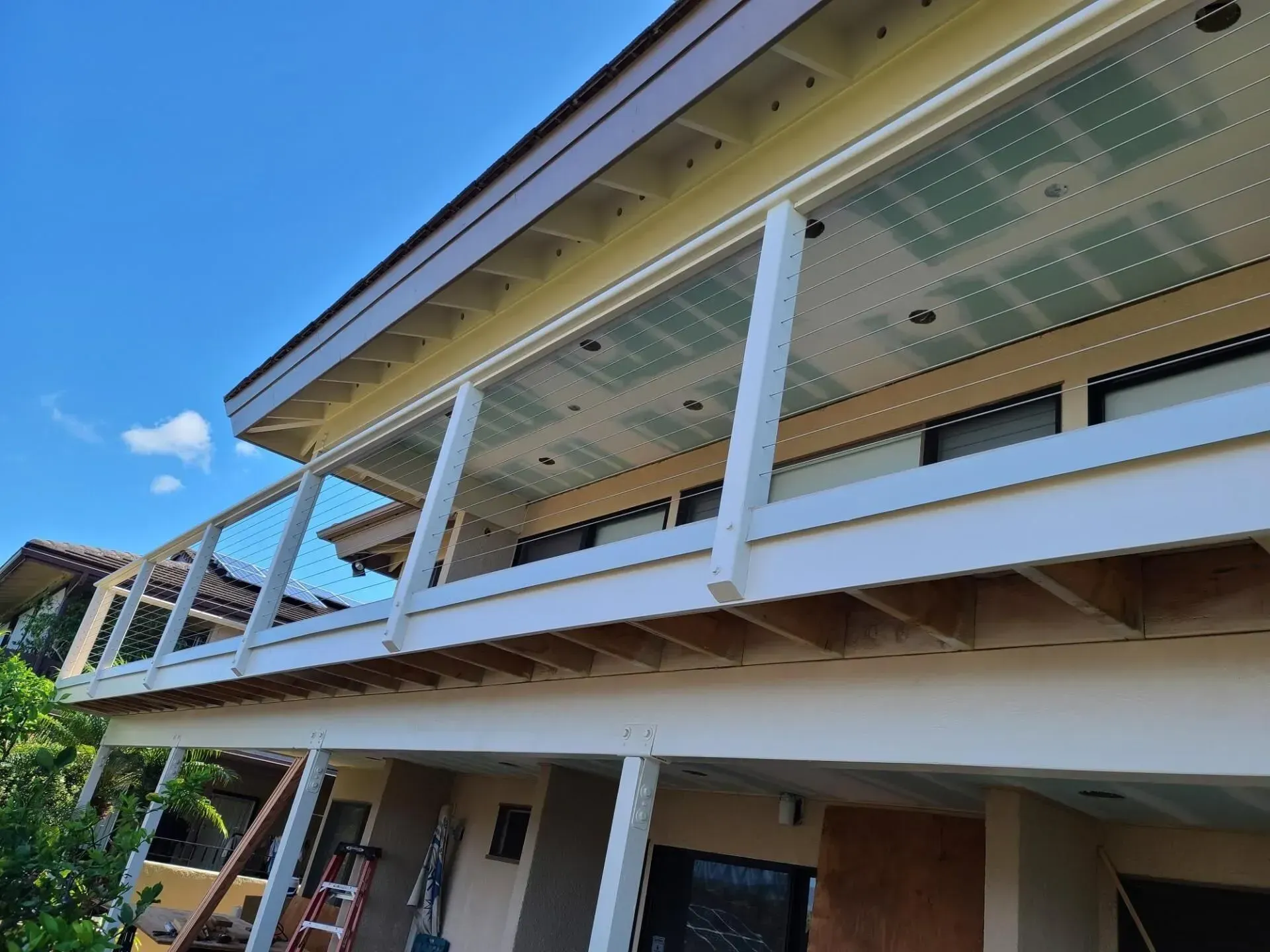 Exterior of a two-story home with a deck. White railing, brown roof, blue sky, and green foliage.