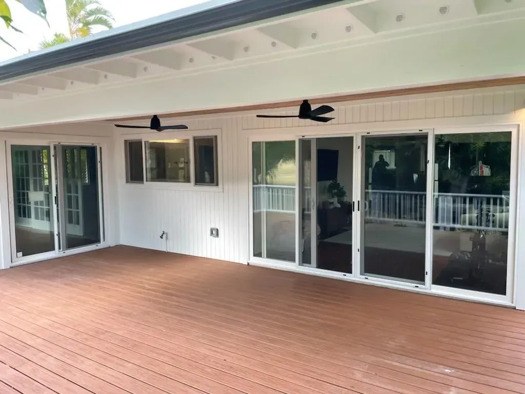 Back patio with brown deck, white siding, and sliding glass doors. Two black ceiling fans.