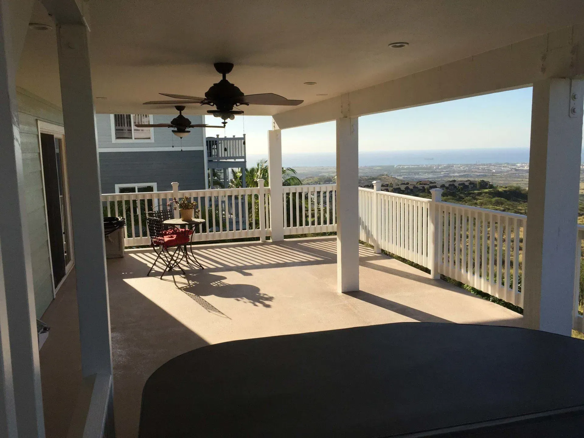Covered patio with a view; features white railing, ceiling fans, and a hot tub.