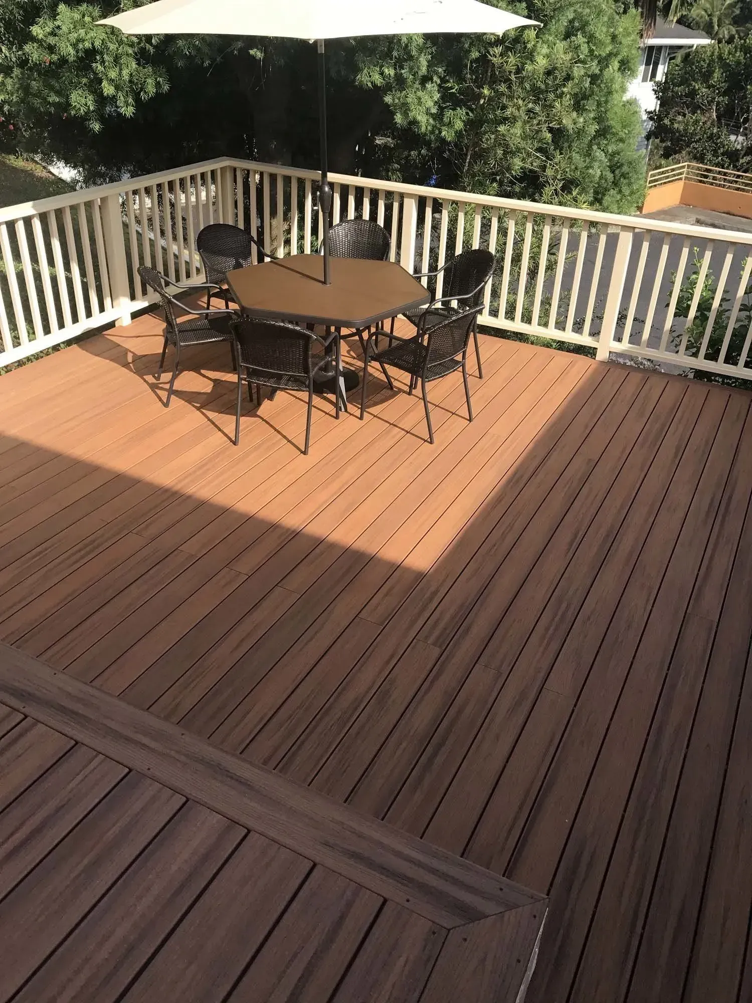 Wooden deck with table, chairs, and umbrella, surrounded by white railing, and trees in the background.