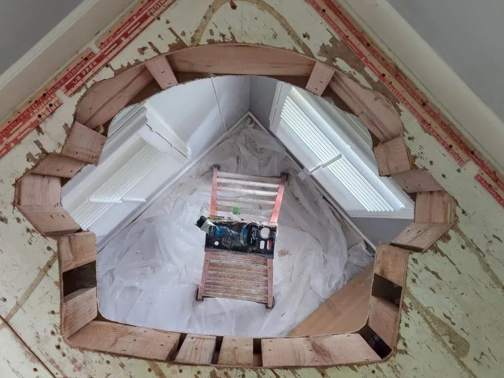 Looking up at a window frame, wooden and unfinished, with a ladder and tools visible through the opening.