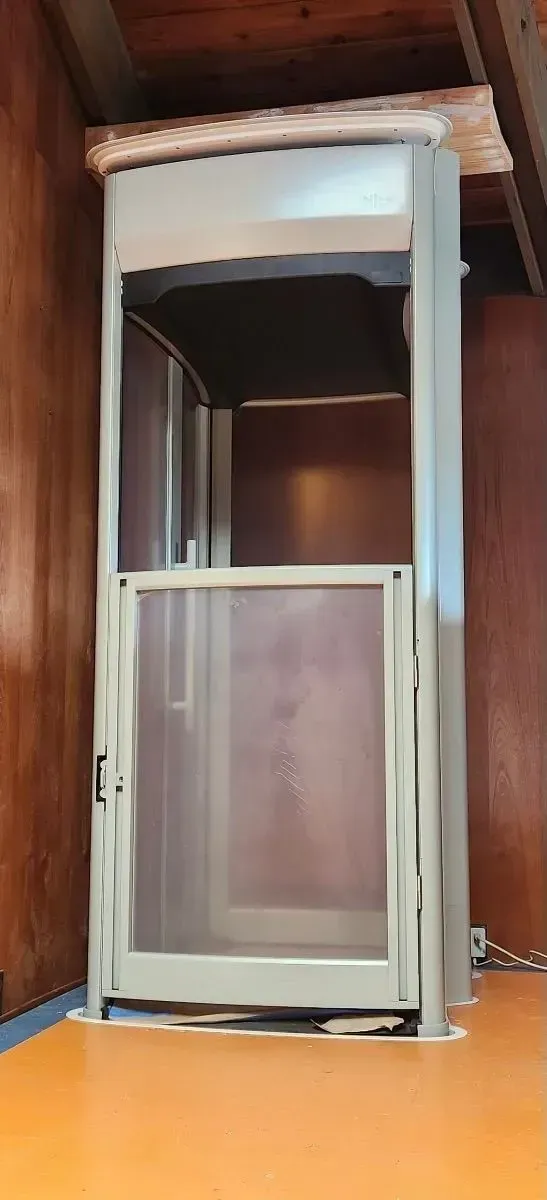 Elevator inside a room. The walls are brown. The floor is orange. The elevator has a see-through door.