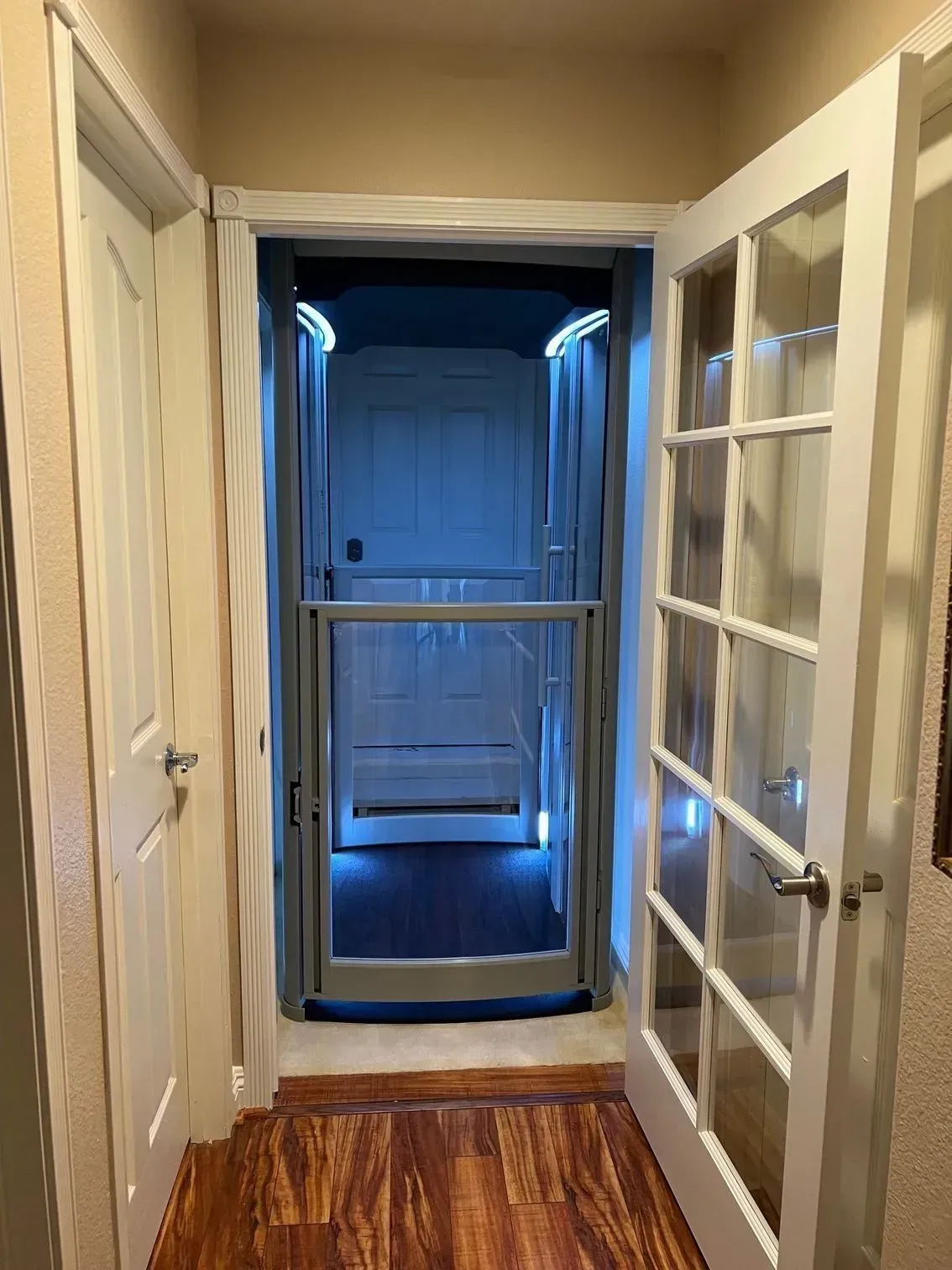 Hallway with open French doors leading to a home elevator, lit with blue lights. Wooden floor.