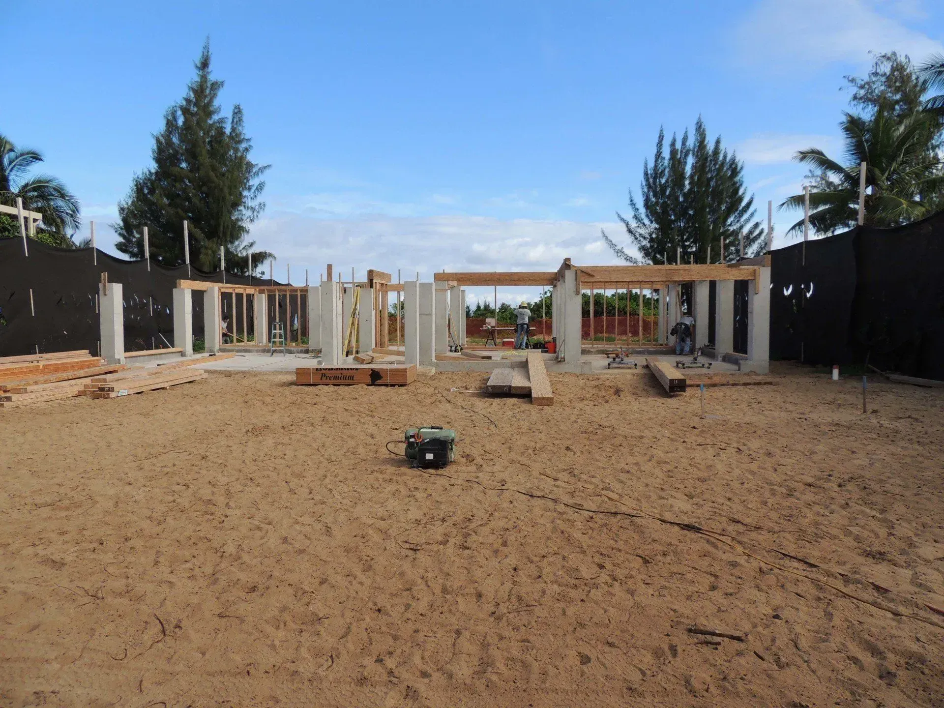 Construction site with concrete columns and wooden frames; sandy ground.