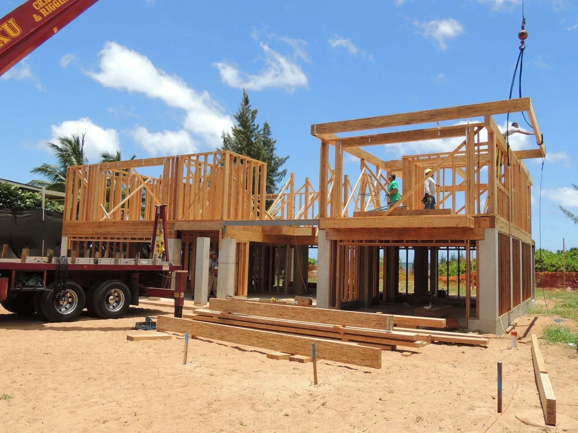 Wood frame house under construction, with a crane lifting a section on a sunny day.