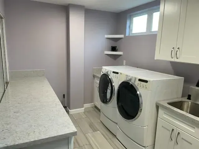 Laundry room with light purple walls, white cabinets, light gray countertop, and washer/dryer.
