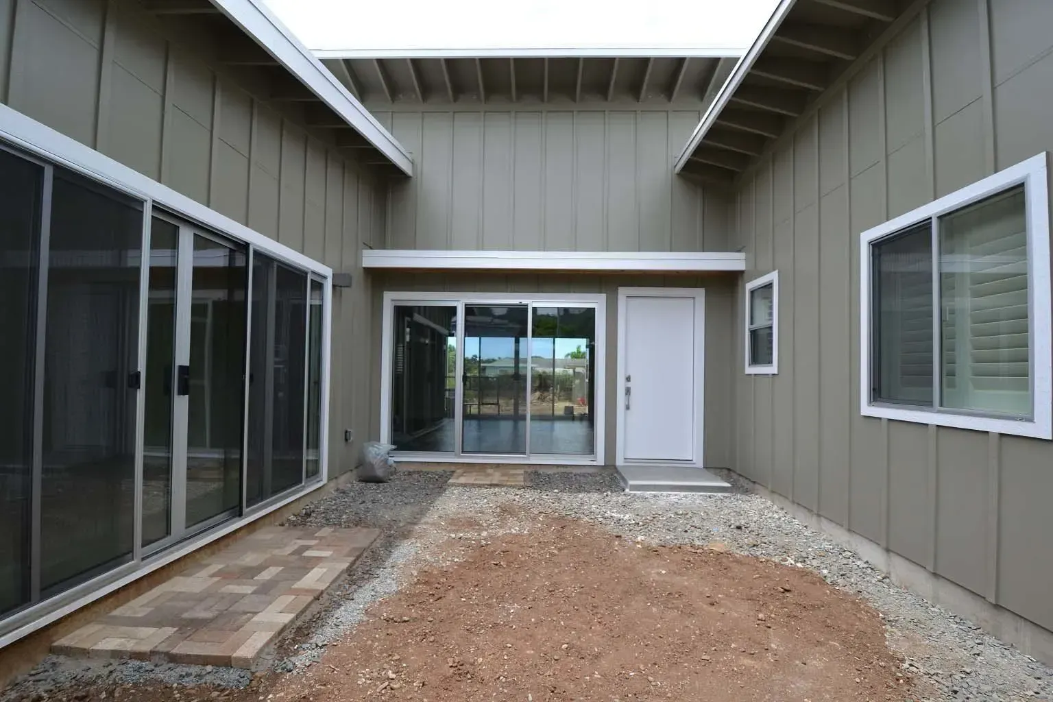 Courtyard with sliding glass doors, a white door, and gravel ground. The walls are a muted green color.