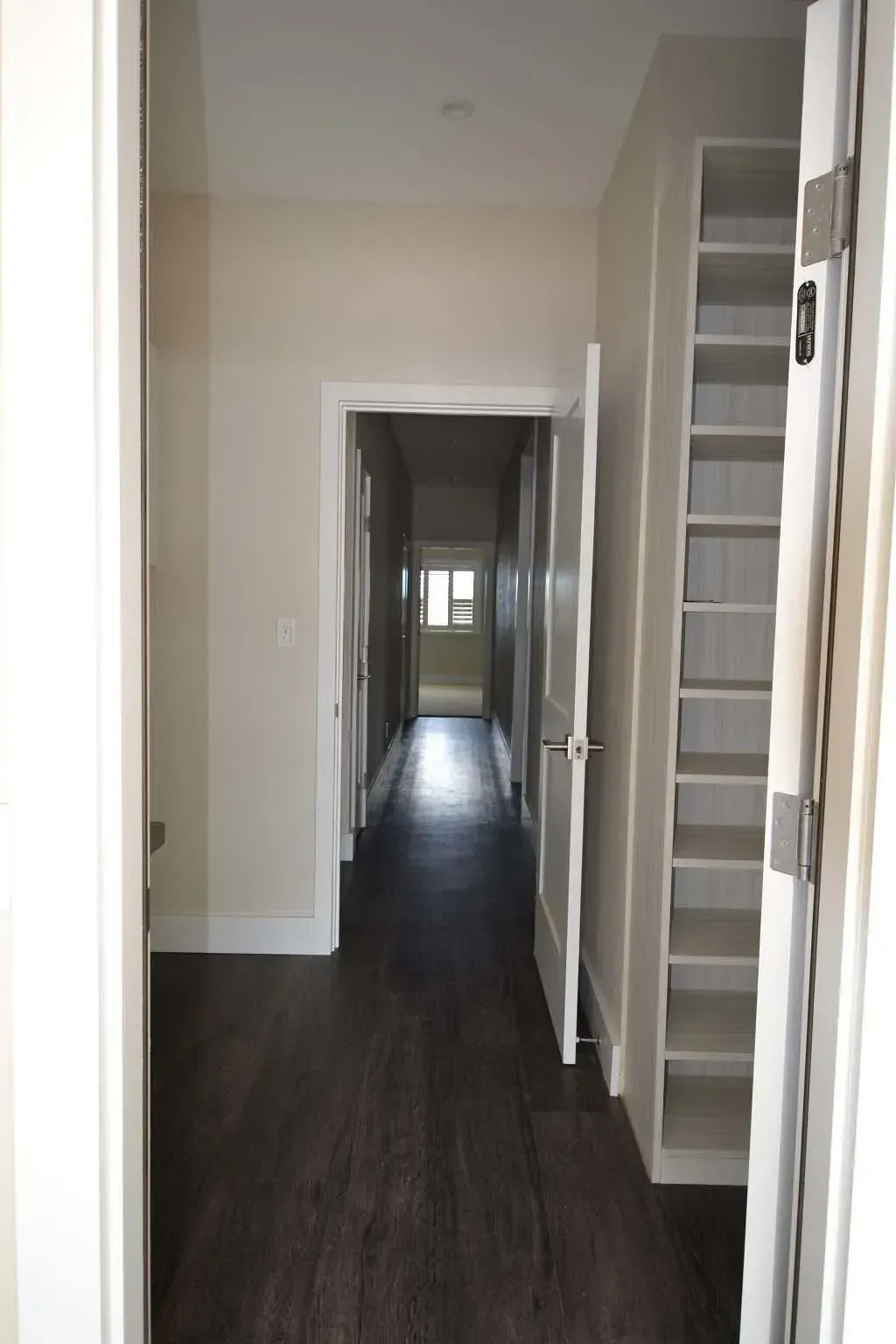 Long hallway with dark wood floors, white walls, and a built-in shelf.