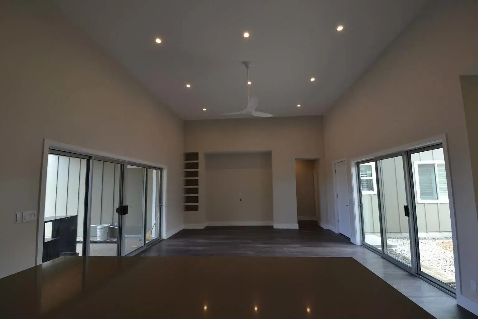 Empty, modern living room with sliding glass doors, recessed lighting, and a ceiling fan.